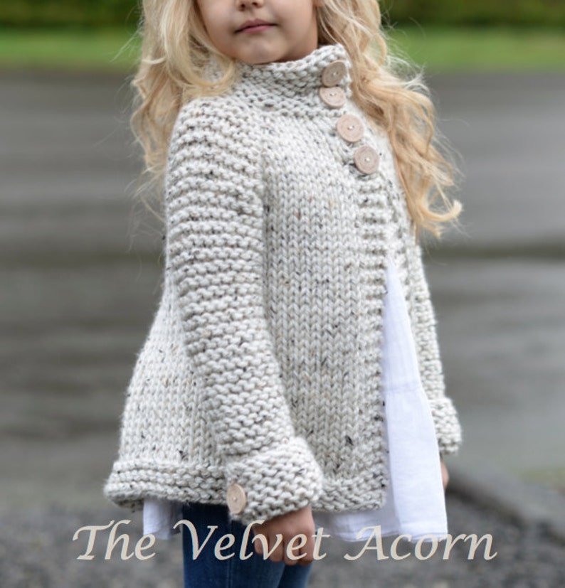 Pu&ograve; includere: Un cardigan di maglia bianco con collo alto e chiusura con bottoni. Il cardigan ha una texture macchiettata e bottoni in legno.
