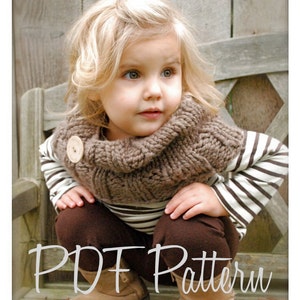 May include: A young child wearing a brown knitted cowl neck scarf with a wooden button. The child is wearing a striped shirt and brown pants. The child is sitting on a wooden bench.  PDF Pattern.