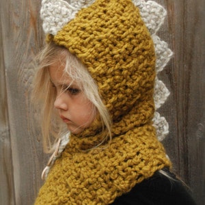 May include: A crocheted dinosaur hooded scarf in mustard yellow and white. The scarf has a pointed hood with a dinosaur-shaped back and a matching scarf.