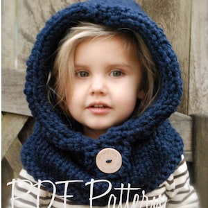 May include: A navy blue knitted hooded cowl with a wooden button. The cowl is worn by a child with blonde hair.