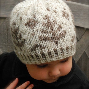 May include: A knitted baby hat with a brown and white geometric pattern. The hat is worn by a baby with brown hair and brown eyes. The text "PDF Pattern" is visible at the bottom of the image.