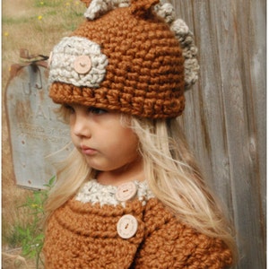 Puede incluir: Un gorro y un cuello a juego de punto de ganchillo marrón y crema con botones de madera. El gorro tiene un diseño de cabeza de caballo con orejas. El gorro y el cuello son un patrón PDF.
