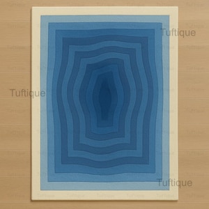 Pode incluir: Um tapete retangular com um design azul em camadas. O tapete apresenta uma série de retângulos concêntricos e ondulados em tons de azul, criando um efeito tridimensional. O tapete é delimitado por uma moldura creme. A palavra "Tuftique" está impressa no tapete.