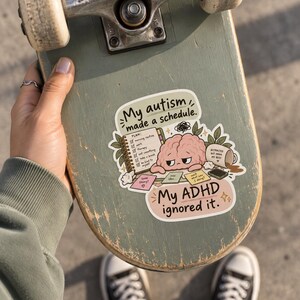 May include: A sticker on a skateboard featuring a cartoon brain with a tired expression resting on a checklist. The text reads My autism made a schedule. My ADHD ignored it. The illustration includes a spilled coffee mug, sticky notes, and a spiral notebook on a light background.