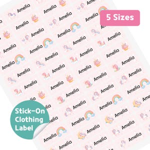 Puede incluir: Una hoja de etiquetas adhesivas rosas para ropa con el nombre "Amelia" impreso en negro. Las etiquetas presentan ilustraciones de unicornios y arcoíris. El texto "5 Sizes" está en un rectángulo rosa. Las palabras "Stick-On Clothing Label" están en un círculo verde.