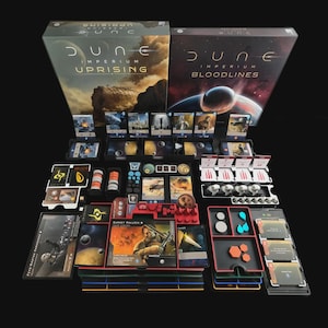 May include: A board game set with two boxes labelled "Dune Imperium Uprising" and "Dune Imperium Bloodlines." The game components include cards, tokens, and player pieces, arranged on a black surface. The game features a sci-fi theme.