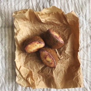 Peut inclure: Trois objets bruns de forme ovale, avec des surfaces texturées et des accents jaunes et violets, présentés sur du papier brun froissé. Les objets ont une apparence réaliste, suggérant un produit naturel.