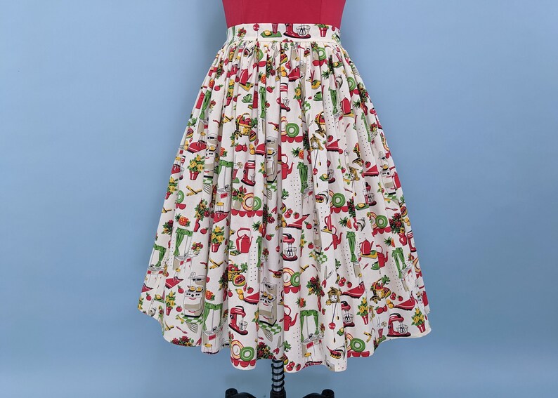 May include: A white full skirt with a red, green and yellow print of kitchen appliances and food. The skirt has a gathered waist and a full, flowing silhouette.