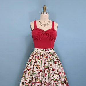May include: A red, strapless top with a twist detail at the bust, paired with a white skirt featuring a colourful print of various kitchen appliances and food items.