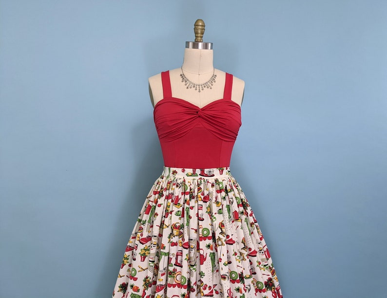 May include: A red, strapless top with a twist detail at the bust, paired with a white skirt featuring a colourful print of various kitchen appliances and food items.