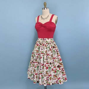 May include: A red, strapless top with a twist detail at the front, paired with a white skirt featuring a vintage-inspired print of kitchen appliances and food. The skirt is full and has a gathered waist.