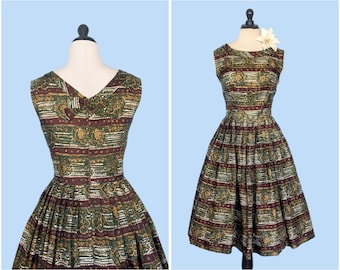 May include: A sleeveless green and brown patterned dress with a white flower accent. The dress has a fitted bodice and a full skirt.