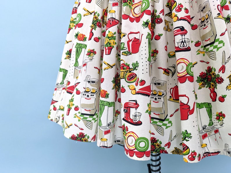May include: A white cotton fabric with a red, green and yellow kitchen-themed print. The print features images of kitchen appliances, food and flowers.