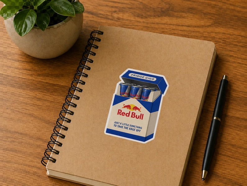 May include: A rectangular sticker featuring a blue and white cigarette pack design labelled Fridge Cigs. The pack contains small blue and silver energy drink cans and displays the Red Bull logo with the text Just a little something to take the edge off.