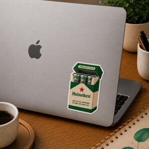 Peut inclure: Un autocollant repr&eacute;sentant une bo&icirc;te de bi&egrave;re Heineken &eacute;tiquet&eacute;e "Fridge Cigs" avec de petites canettes de bi&egrave;re vertes &agrave; l'int&eacute;rieur. La bo&icirc;te est verte et blanche avec une &eacute;toile rouge.