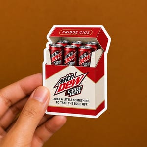 May include: A die-cut sticker shaped like a red and white cigarette pack containing six miniature red soda cans labeled Mtn Dew Code Red. The pack features the text FRIDGE CIGS at the top, the Mtn Dew Code Red logo, and the phrase JUST A LITTLE SOMETHING TO TAKE THE EDGE OFF.