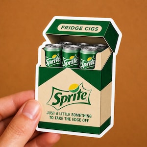 May include: A die-cut sticker shaped like a cigarette pack, colored dark green and tan. The top flap reads FRIDGE CIGS. Inside are green soda cans labeled Sprite. The front features the Sprite logo and the text JUST A LITTLE SOMETHING TO TAKE THE EDGE OFF.
