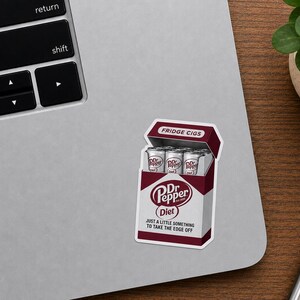 May include: A rectangular sticker featuring a maroon and white box design that mimics a cigarette pack. The box is labeled FRIDGE CIGS at the top and contains silver soda cans. It features the Dr Pepper Diet logo and the text JUST A LITTLE SOMETHING TO TAKE THE EDGE OFF.
