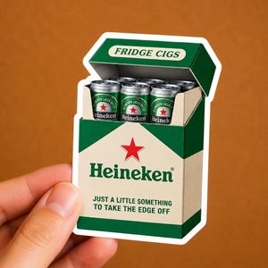 Peut inclure: Un autocollant en forme de paquet de cigarettes, intitul&eacute; "FRIDGE CIGS", rempli de mini canettes de bi&egrave;re Heineken. La bo&icirc;te est verte et blanche, avec le logo Heineken et le texte "JUST A LITTLE SOMETHING TO TAKE THE EDGE OFF."