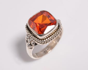 Könnte beinhalten: Ein Silberring mit einem großen, quadratisch geschliffenen, orangefarbenen Edelstein. Der Ring hat ein detailliertes, geflochtenes Design um den Edelstein und ein glattes Band. Der Ring ist ein Schmuckstück.