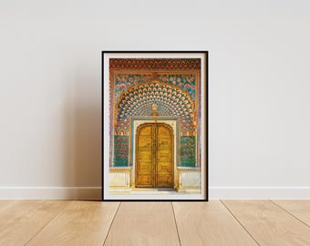 May include: Framed print of a golden arched doorway with intricate, colorful patterns. The doorway is set against a backdrop of teal and red floral designs, with a peacock feather arch. The print is in a black frame.