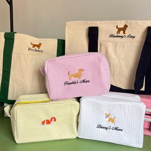K&ouml;nnte beinhalten: Eine Auswahl an Taschen und Beuteln zum Thema Hunde aus Canvas und Seersucker. Die Taschen sind in Beige, Rosa, Gelb und Wei&szlig; erh&auml;ltlich. Jede Tasche hat ein gesticktes Hundedesign und einen Namen. Enth&auml;lt Tragetaschen und Rei&szlig;verschlusstaschen.