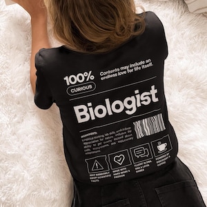 Może przedstawiać: Czarny t-shirt z napisem "Biologist" w kolorze białym, tekstem "100% Curious" i ikonami naukowymi. Koszulka zawiera również tekst "Contents may include an endless love for life itself."