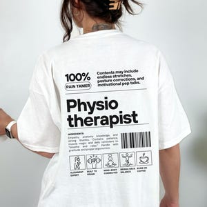 May include: White t-shirt with the words "Physio Therapist" in large black letters. The shirt also features text that reads "100% Pain Tamer" and a list of ingredients. The shirt has a relaxed fit.
