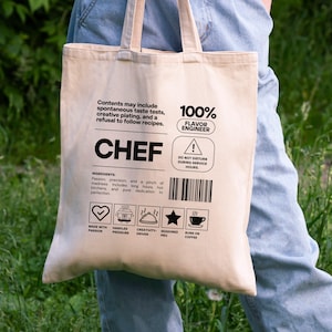 Puede incluir: Una bolsa de lona beige con texto y gráficos en negro. El texto incluye "CHEF", "100% FLAVOR ENGINEER" y detalles de ingredientes. La bolsa presenta iconos y frases como "Runs on Coffee".