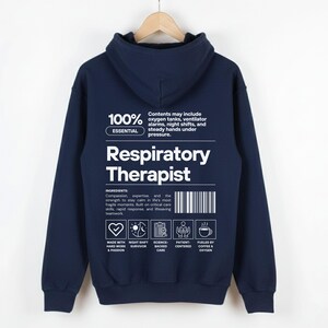 Może przedstawiać: Granatowa bluza z kapturem z białym napisem "Respiratory Therapist". Tył bluzy z kapturem zawiera listę składnik&oacute;w i ikony. Bluza z kapturem wisi na drewnianym wieszaku.