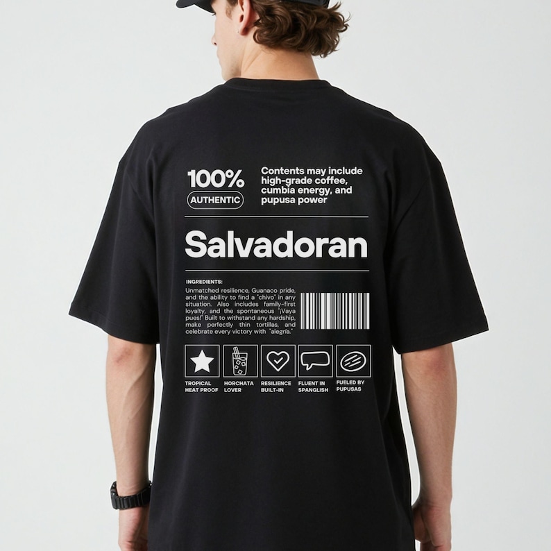 Pu&ograve; includere: T-shirt nero con testo e grafica bianchi. La maglietta presenta la parola "Salvadoran" e il testo "100% Authentic". Il testo aggiuntivo include ingredienti e icone. &Egrave; un capo casual.