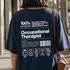 Może przedstawiać: Granatowa koszulka z białym napisem "Occupational Therapist". Koszulka zawiera listę składników i ikony. Widoczny jest również tekst "100% Life Skills Pro".