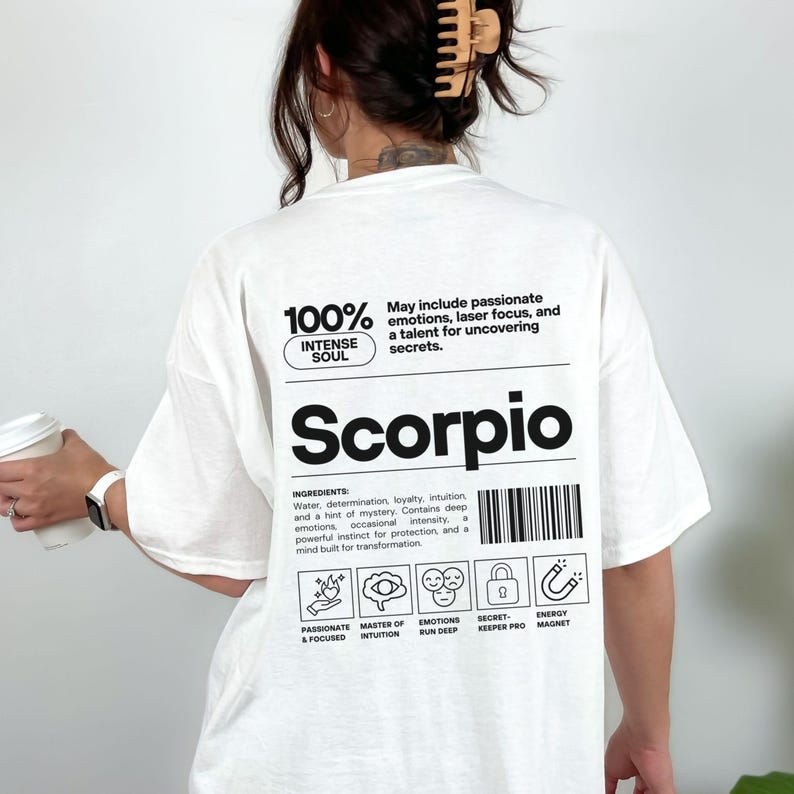 Pode incluir: Camiseta branca com a palavra "Scorpio" em letras pretas grandes. A camiseta apresenta texto sobre os tra&ccedil;os de Escorpi&atilde;o, incluindo "Intense Soul" e "Passionate & Focused". A camiseta tamb&eacute;m tem um design de c&oacute;digo de barras.