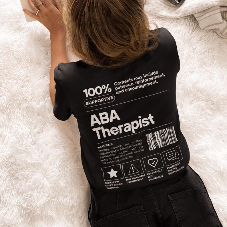 K&ouml;nnte beinhalten: Schwarzes T-Shirt mit dem Text "ABA Therapist" in Wei&szlig;. Das Shirt enth&auml;lt die Worte "100% Supportive" und andere Texte &uuml;ber die Inhaltsstoffe eines ABA-Therapeuten. Das Shirt hat auch Symbole und S&auml;tze.