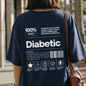 Op de afbeelding: Marineblauw t-shirt met het woord "Diabetic" in grote witte letters. Het shirt bevat tekst over ingrediënten en symbolen voor glucosemonitoring en insuline. Het shirt heeft ook de tekst "100% Sweet".