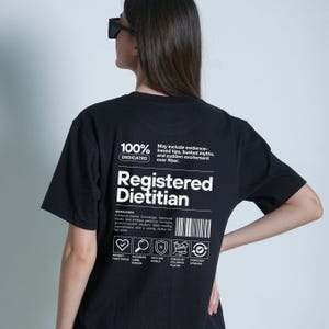 Pu&ograve; includere: T-shirt nero con la scritta bianca "Registered Dietitian". La maglietta presenta anche la scritta "100% Dedicated" e un elenco di ingredienti. &Egrave; un capo casual.