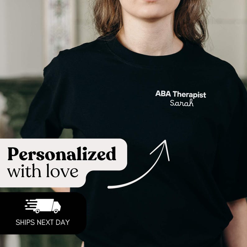K&ouml;nnte beinhalten: Schwarzes Rundhals-T-Shirt mit dem wei&szlig;en Text "ABA Therapist Sarah". Der Satz "Personalisiert mit Liebe" wird in einer wei&szlig;en Sprechblase angezeigt. Ein wei&szlig;er Pfeil zeigt auf das T-Shirt. Ein einfaches, allt&auml;gliches Kleidungsst&uuml;ck.