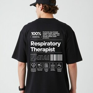 Może przedstawiać: Czarny t-shirt z białym napisem "Respiratory Therapist". Koszulka zawiera tekst "100% Essential" i listę składnik&oacute;w. Dodatkowy tekst to "Made with hard work & passion" i "Fueled by coffee & oxygen."