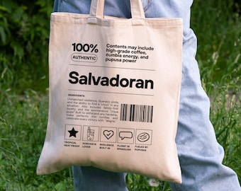 May include: Beige canvas tote bag with the word "Salvadoran" in large black letters. The bag includes text about ingredients and icons. The text reads "100% Authentic" and "Contents may include high-grade coffee, cumbia energy, and pupusa power."