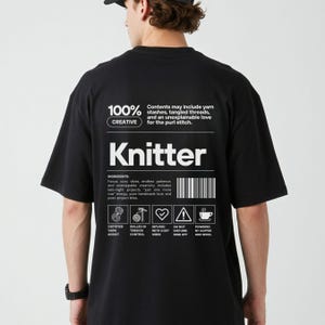 Op de afbeelding: Zwart t-shirt met het woord "Knitter" in het wit. Het shirt heeft een afbeelding met ingredi&euml;nten zoals "cozy vibes" en "endless patience". Het shirt heeft ook de tekst "100% Creative".