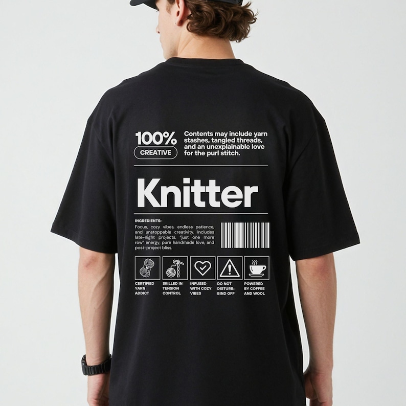 Op de afbeelding: Zwart t-shirt met het woord "Knitter" in het wit. Het shirt heeft een afbeelding met ingredi&euml;nten zoals "cozy vibes" en "endless patience". Het shirt heeft ook de tekst "100% Creative".
