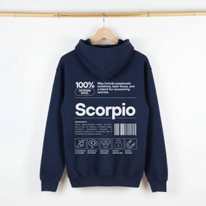 Pode incluir: Moletom azul marinho de Escorpi&atilde;o com texto branco. A parte de tr&aacute;s do moletom com capuz apresenta a palavra "Escorpi&atilde;o", o texto "100% Intense Soul" e outro texto que descreve os tra&ccedil;os de Escorpi&atilde;o. O moletom com capuz tem capuz e cord&atilde;o.