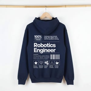 May include: Navy blue hoodie with the text "Robotics Engineer" in white. The back of the hoodie features a list of "ingredients" and icons. The hoodie is hanging on a wooden hanger against a white background.