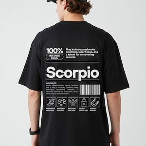Pode incluir: Camiseta preta com texto e gr&aacute;ficos brancos. A camiseta apresenta a palavra "Scorpio" e a frase "100% Intense Soul". Texto adicional descreve os tra&ccedil;os de Escorpi&atilde;o e inclui &iacute;cones. H&aacute; tamb&eacute;m um c&oacute;digo de barras.