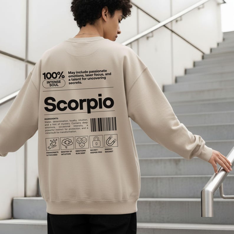 Pode incluir: Camisola bege com a palavra "Scorpio" impressa em preto. A parte de tr&aacute;s da camisola apresenta texto sobre os tra&ccedil;os de Escorpi&atilde;o, incluindo "alma intensa" e "emo&ccedil;&otilde;es apaixonadas". O design inclui um c&oacute;digo de barras e v&aacute;rios &iacute;cones.