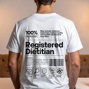 Pu&ograve; includere: T-shirt bianca con la scritta "Registered Dietitian" in un design nero in stile codice a barre. La maglietta include le parole "100% Dedicated" e un elenco di ingredienti relativi alla nutrizione e alla salute. La maglietta ha anche delle icone.