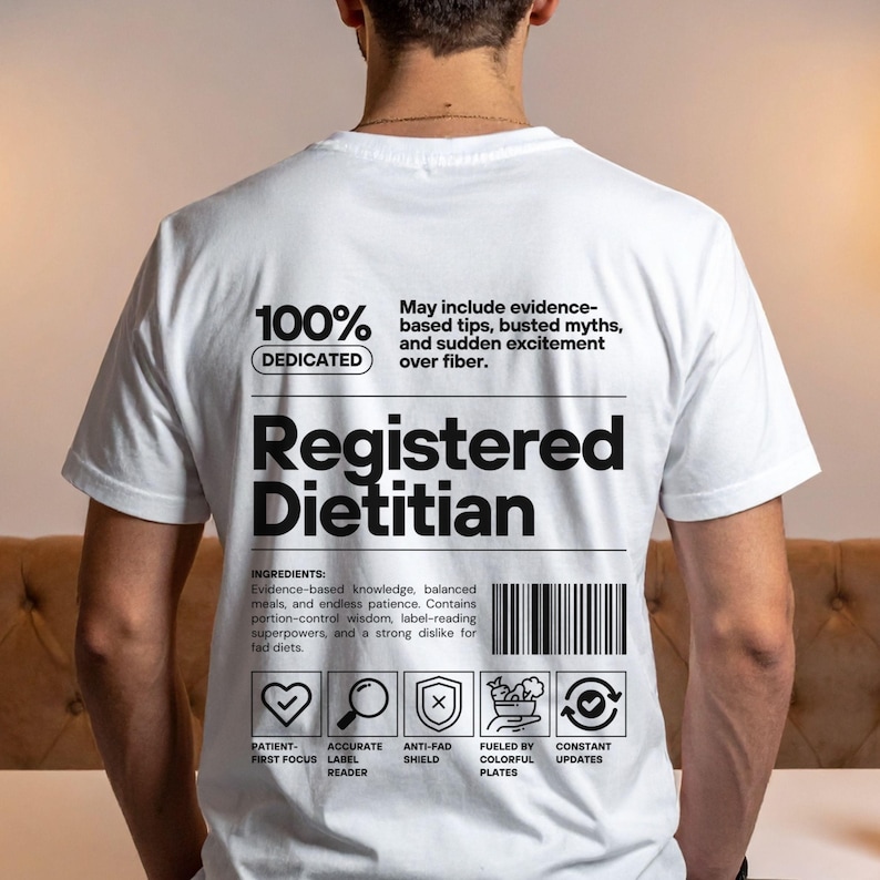 Pu&ograve; includere: T-shirt bianca con la scritta "Registered Dietitian" in un design nero in stile codice a barre. La maglietta include le parole "100% Dedicated" e un elenco di ingredienti relativi alla nutrizione e alla salute. La maglietta ha anche delle icone.