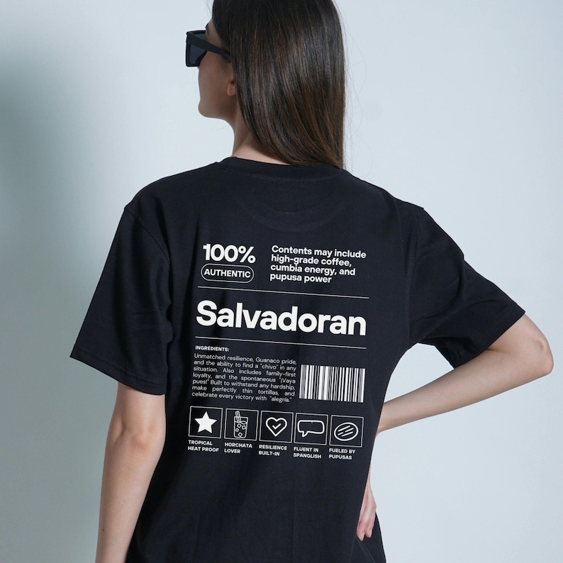 Pu&ograve; includere: T-shirt nero con testo bianco "Salvadoran". La maglietta include un elenco di ingredienti e icone. Il testo "100% Authentic" &egrave; stampato anche sulla maglietta.