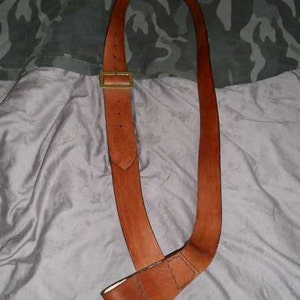 May include: A brown leather strap with a brass buckle. The strap is folded in half and has a loop at one end.