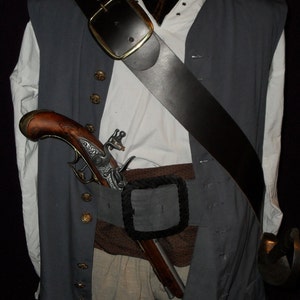 May include: A pirate costume comprising a grey waistcoat over a white shirt, a brown belt, and a black shoulder strap. A decorative pistol is tucked into the belt, and a sword is visible. The costume includes tan trousers.